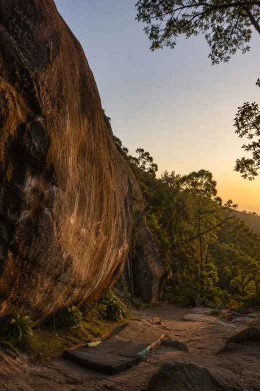 Parede de rocha com trilha e mata ao pôr do sol
